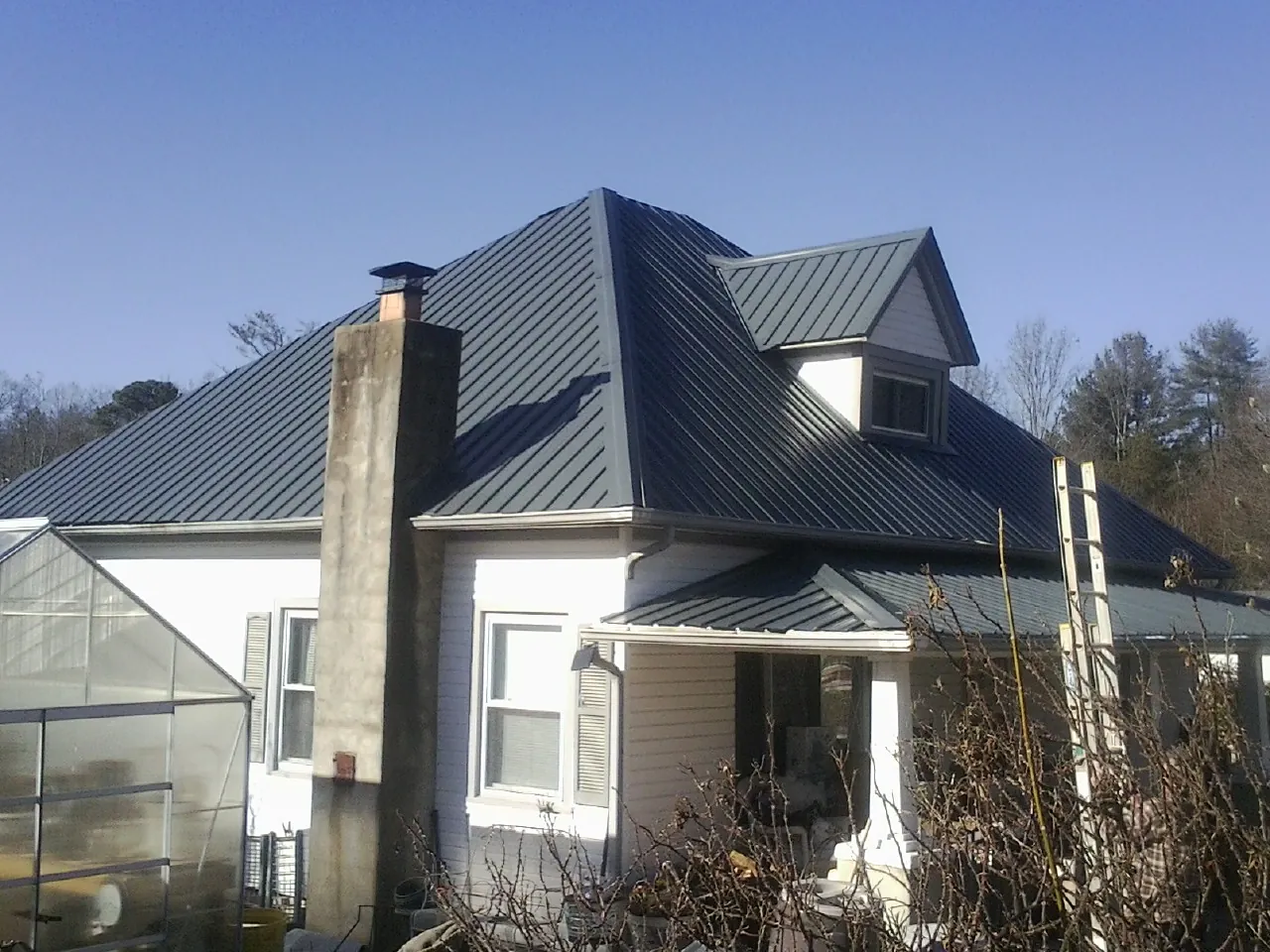 Dark blue standing seam metal roof on a white farmhouse with dormer — Slate & Tile Roof Repair by Roofing Brothers in Lake Placid