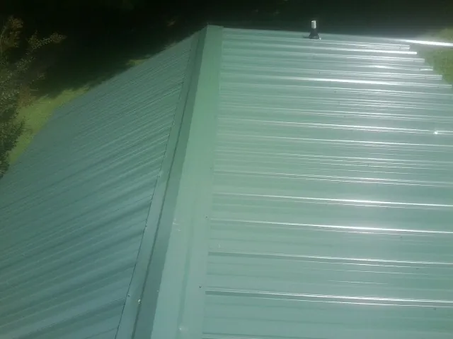 New green metal panels meeting at the ridge of a roof — Flat Roof Repair work by our crew in Lake Placid