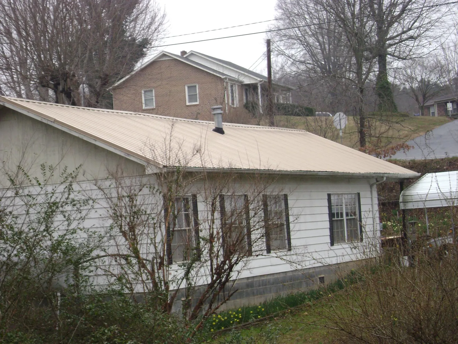 Tan metal roof on a white sided house set into a hillside — Commercial Roofing by Roofing Brothers in Lake Placid